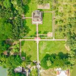 Aerial view of a grand mansion with formal gardens, lawns, pathways, and water bodies, illustrating the concept of being house rich cash poor in wealth management
