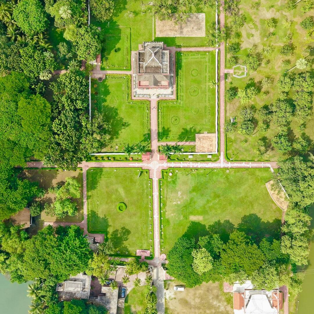 Vista aérea de una gran mansión con jardines formales, céspedes, senderos y cuerpos de agua, ilustrando el concepto de ser rico en bienes pero pobre en liquidez en gestión de patrimonio