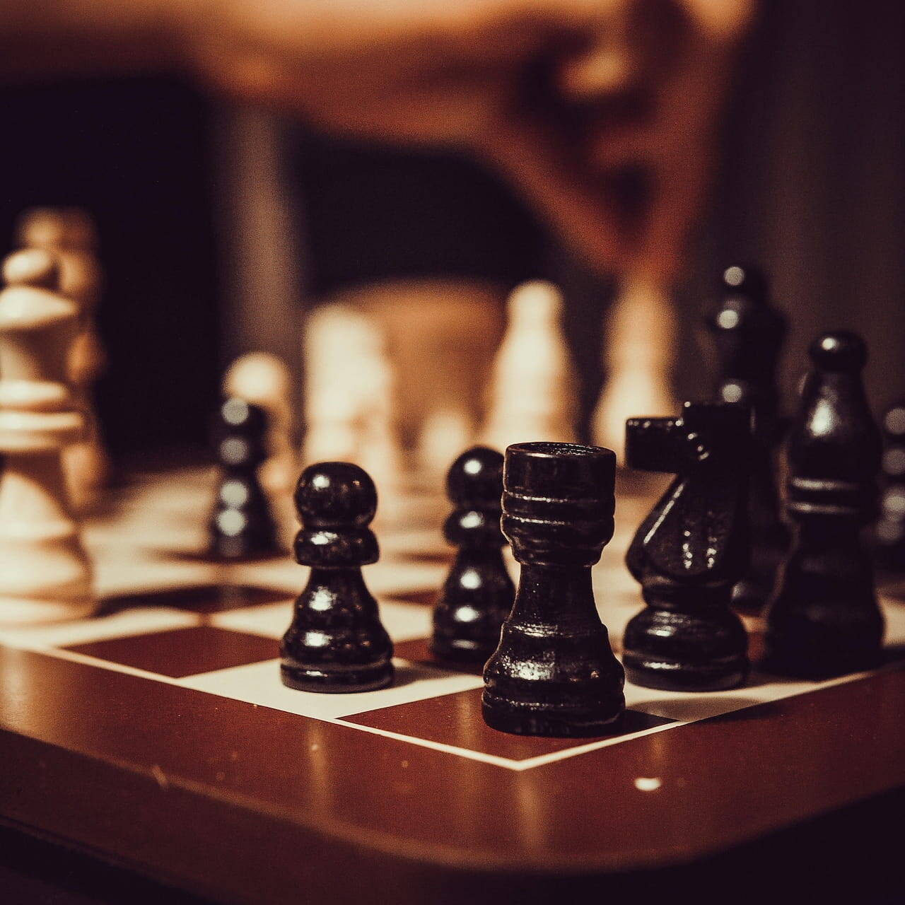 Foto en primer plano de un tablero de ajedrez con piezas blancas y negras, una mano moviendo una pieza, representando la toma de decisiones estratégicas en inversión y mitigación de riesgos geopolíticos.