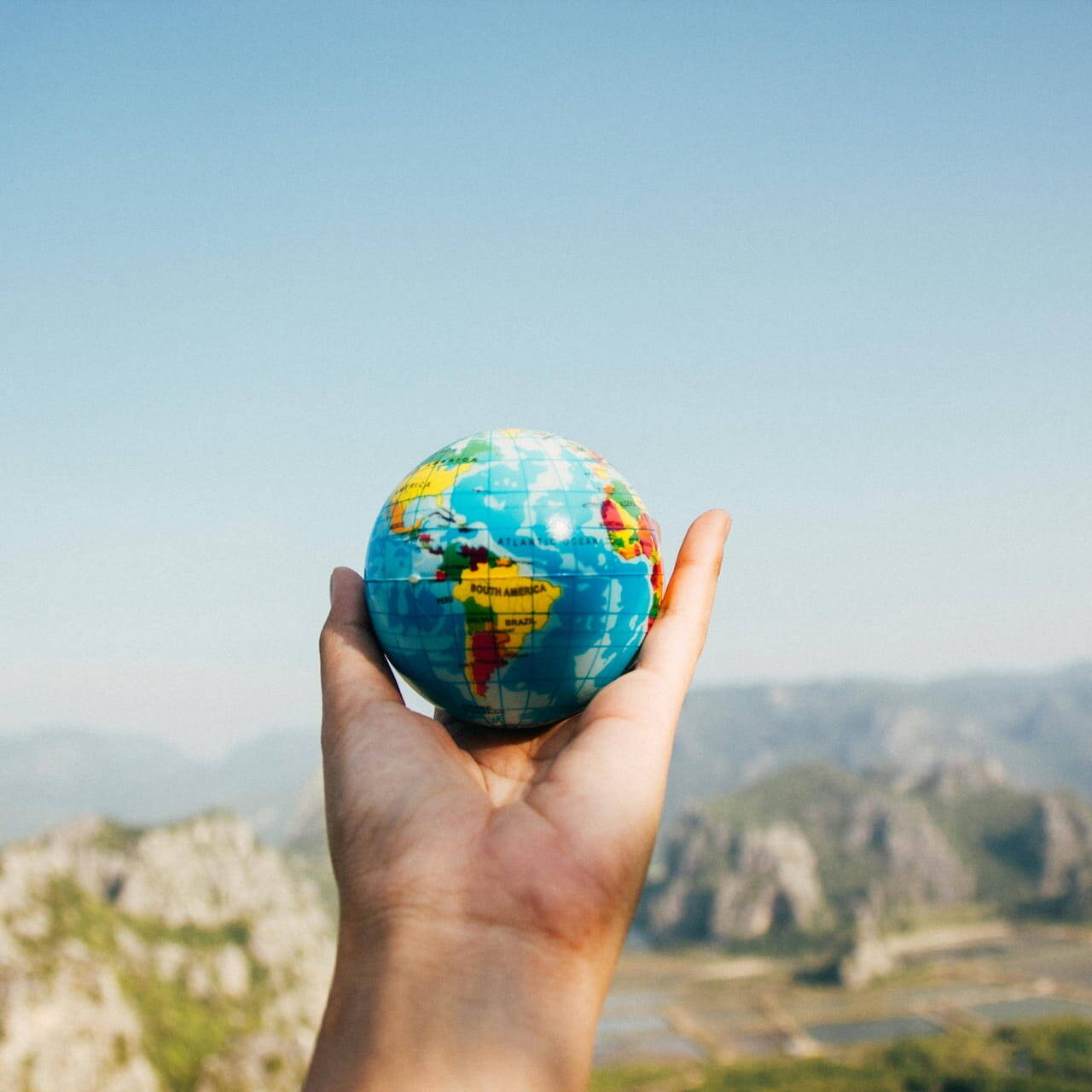 Main tenant un globe terrestre contre un fond montagneux, symbolisant l'internationalisation du patrimoine familial et la diversification mondiale des actifs.