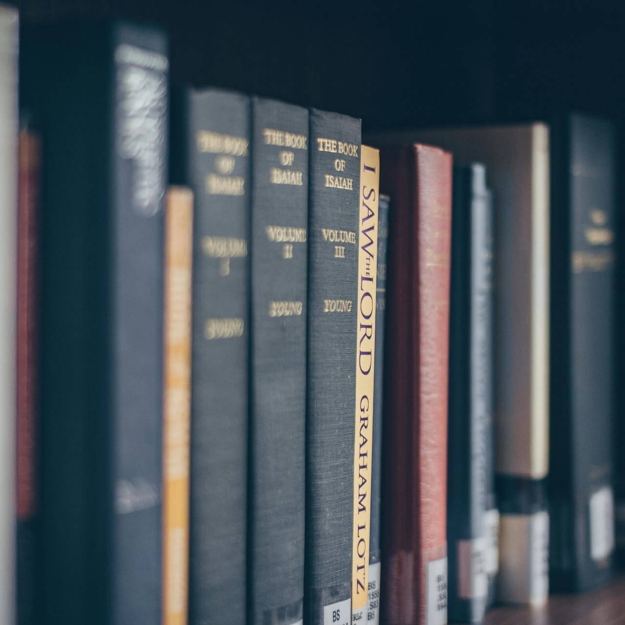Primer plano de libros en una estantería de biblioteca que incluye volúmenes sobre Isaías y obras de Graham Lotz, evocando el concepto de conocimiento preservado y legados familiares en la gestión patrimonial.